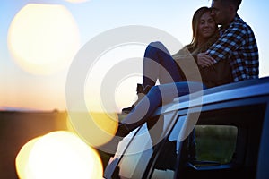 Loving couple embracing and sitting on car