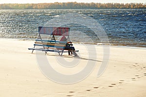 Loving couple embracing sitting on a wooden bench, enjoying the view of the river and the waves on a windy Sunny day