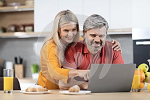 Loving couple enjoying healthy breakfast, using computer, kitchen interior