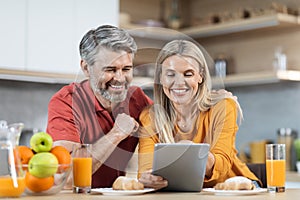 Loving couple enjoying healthy breakfast, using digital tablet