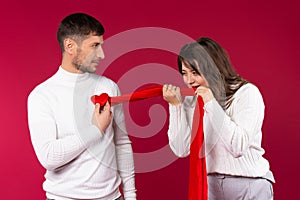 A loving couple fooling around on red background. Lovers pastime concept. Girl snatches the boy`s heart from his chest
