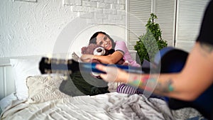 Loving couple with guitar sitting on bed. Man playing blue acoustic guitar while sitting on bed for your girlfriend