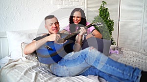 Loving couple with guitar sitting on bed. Man playing blue acoustic guitar while sitting on bed for your girlfriend