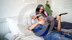 Loving couple with guitar sitting on bed. Man playing blue acoustic guitar while sitting on bed for your girlfriend