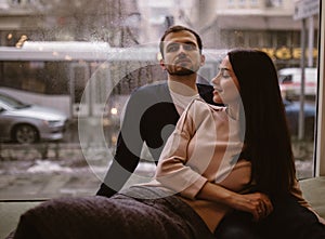 Loving couple. Guy and his girlfriend dressed in in sweaters and jeans sitting close to each other on the windowsill in