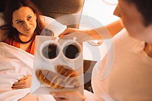 Loving couple having Breakfast in bed with coffee and croissants