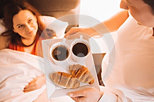 Loving couple having Breakfast in bed with coffee and croissants