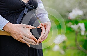 Loving couple with heart shape hands around pregnant belly
