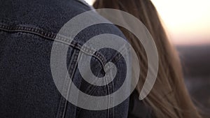 Loving couple holding hands together and embracing while standing on high building roof and watching sunset. Close up