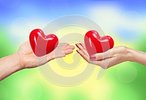 Loving couple holding hearts in hands over bright nature