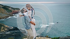 Loving couple hugging coast hill. Happy man spinning woman near calm ocean view