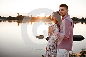 Loving couple hugging on the lake at sunset. Beautiful young couple in love walking on the shore of the lake at sunset in the rays