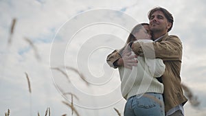 Loving couple hugging standing on the right at background of cloudy autumn sky in wheat field. Happy smiling Caucasian