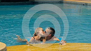 The loving couple hugs and kisses, drinking blue cocktail alcohol liquor in swimming pool at hotel outdoor. Portrait of