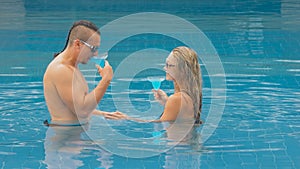 The loving couple hugs and kisses, drinking blue cocktail alcohol liquor in swimming pool at hotel outdoor. Portrait of