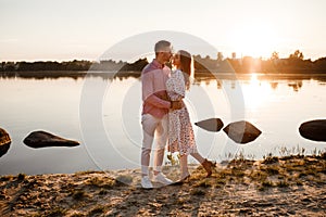 Loving couple kissing on the lake at sunset. Beautiful young couple in love walking on the shore of the lake at sunset in the rays