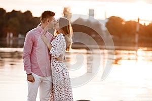 Loving couple kissing on the lake at sunset. Beautiful young couple in love walking on the shore of the lake at sunset in the rays