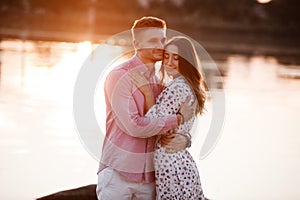 Loving couple look at each other on the lake at sunset. Beautiful young couple in love walking on the shore of the lake at sunset