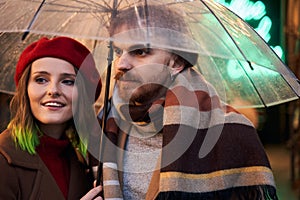 Loving couple looking away while hiding under transparent umbrella