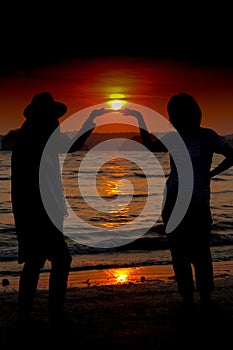 Loving couple make heart shape on beach with the sun set