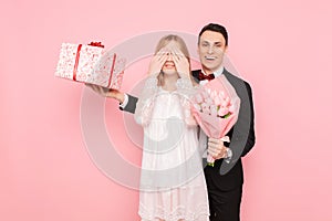 A loving couple, a man gives a shocked woman a bouquet of tulips and a box with a gift on a pink background. Valentine`s Day