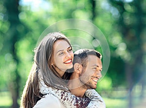 Loving couple man and woman having fun piggybacking in park