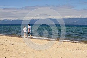 A loving couple of a man and a woman walks along the sand coastline of Lake Baikal on a mountain background on a sunny day.