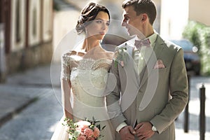 A loving couple of newlyweds walks in the city, and smile. The bride in a beautiful dress, the groom dressed stylishly