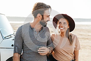 Loving couple outdoors at the beach near car drinking tea