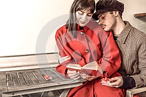 Loving couple reading a book in the bar. Two gifts with red bow are placed on the table