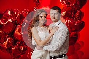 Loving couple with red balloons hearts. Man and woman celebrate valentine`s day. Romantic date on a red background. Boyfriend and