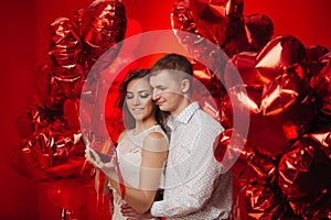 Loving couple with red balloons hearts. Man and woman celebrate valentine`s day. Romantic date on a red background. Boyfriend and