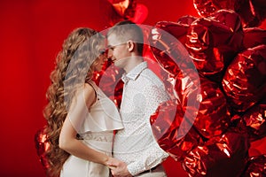 Loving couple with red balloons hearts. Man and woman celebrate valentine`s day. Romantic date on a red background. Boyfriend and