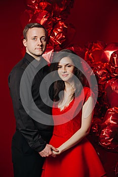 Loving couple with red balloons hearts. Man and woman celebrate valentine`s day. Romantic date on a red background. Boyfriend and