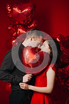 Loving couple with red balloons hearts. Man and woman celebrate valentine`s day. Romantic date on a red background. Boyfriend and