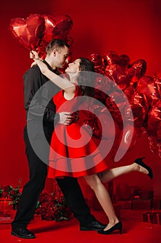 Loving couple with red balloons hearts. Man and woman celebrate valentine`s day. Romantic date on a red background. Boyfriend and