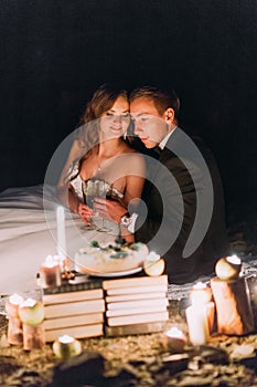 Loving couple share a romantic dinner with candles and cake at beach, coast against wonderful night