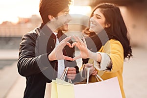 Loving couple showing heart sign with hands, after shopping