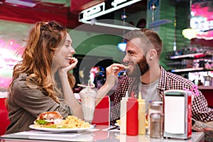 Loving couple sit in retro bright cafe eat french fries indoors