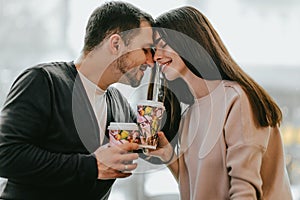 Loving couple is siting face to face on the background of window and holding cups in their hands.