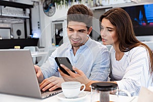 Loving couple sitting in cafe using laptop computer and mobile phone