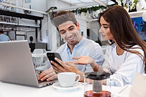 Loving couple sitting in cafe using laptop computer and mobile phone