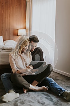 Loving couple sitting on the floor in bedroom and using tablet