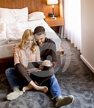 Loving couple sitting on the floor in bedroom and using tablet