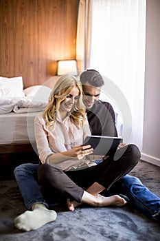 Loving couple sitting on the floor in bedroom and using tablet