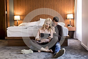 Loving couple sitting on the floor in bedroom and using tablet