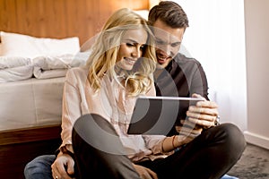 Loving couple sitting on the floor in bedroom and using tablet