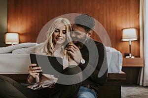Loving couple sitting on the floor in bedroom and using tablet