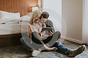 Loving couple sitting on the floor in bedroom and using tablet