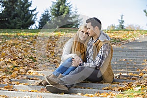 Loving couple sitting together on steps in park during autumn